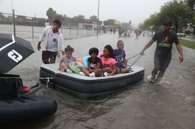 People use an air matress to float down a flooded street as they evacuate their homes after the area was inundated with flooding from Hurricane Harvey on August 27, 2017 in Houston, Texas<br>